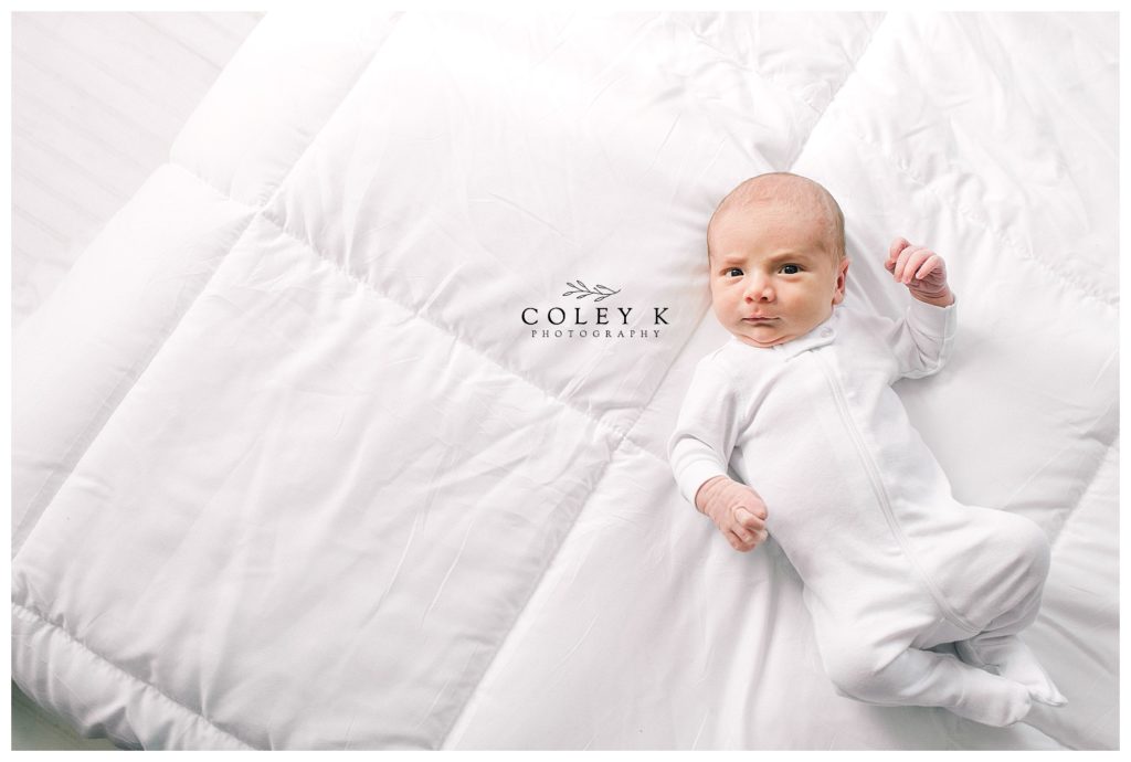 candid newborn photography white onsie on bed