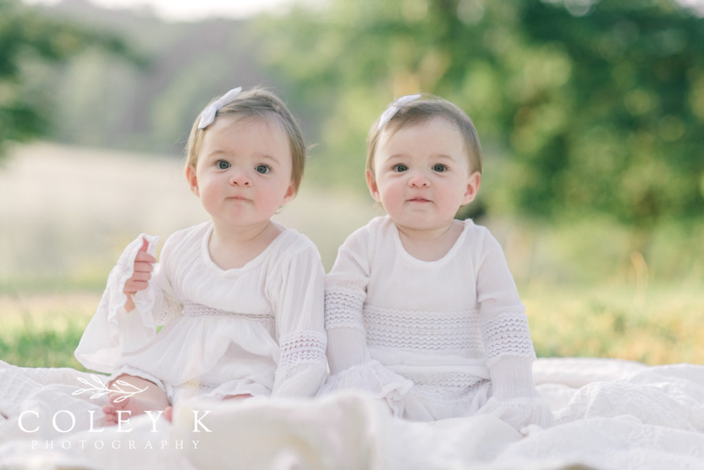 one year old twin girls wearing white dresses by Beaver Lake 